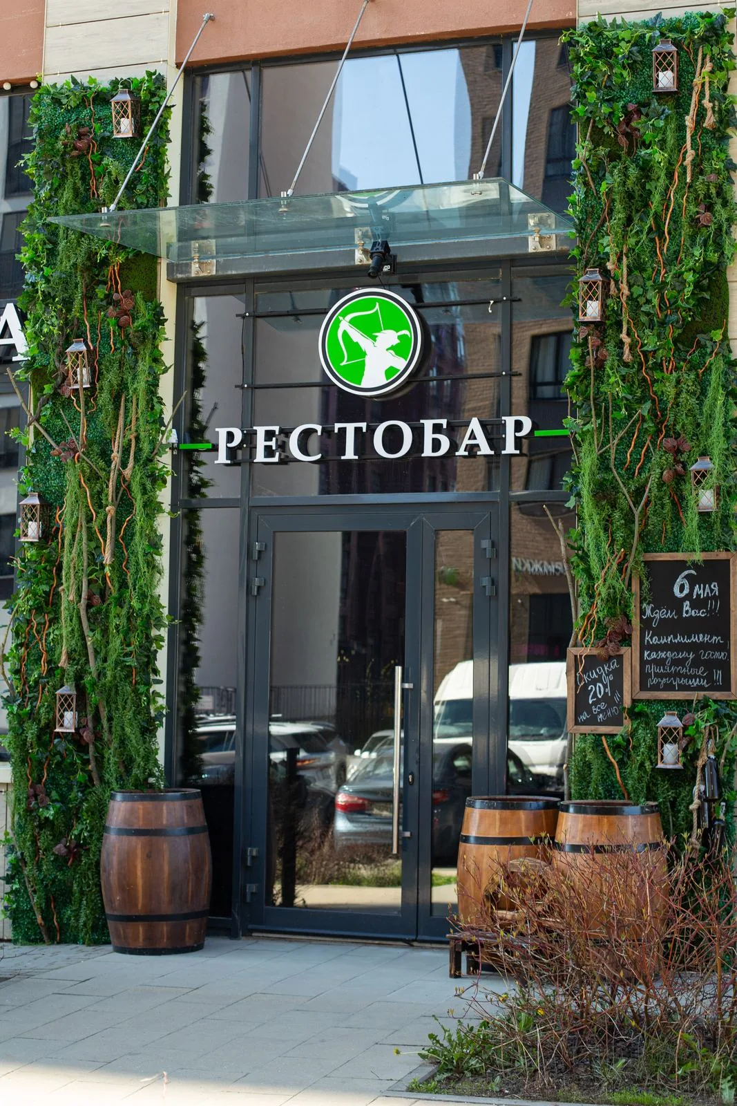 Вход в рестобар: стеклянный козырёк, зелёные стены, бочки